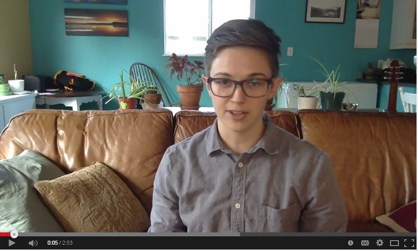Alyx MacAdams, Trans Inclusion Coordinator, sitting on a couch for vlog update